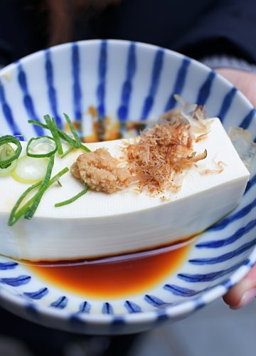 person holding white and blue ceramic plate with rice and sliced cucumber